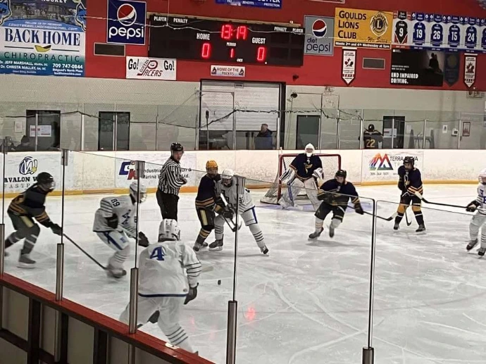 An ice hockey match showing the goaltender and multiple players from both teams.