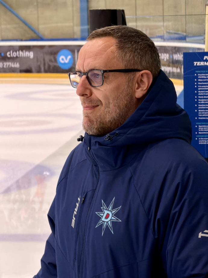 A top half image of ice hockey coach Matt Darlow standing at the side of the rink looking to the left.